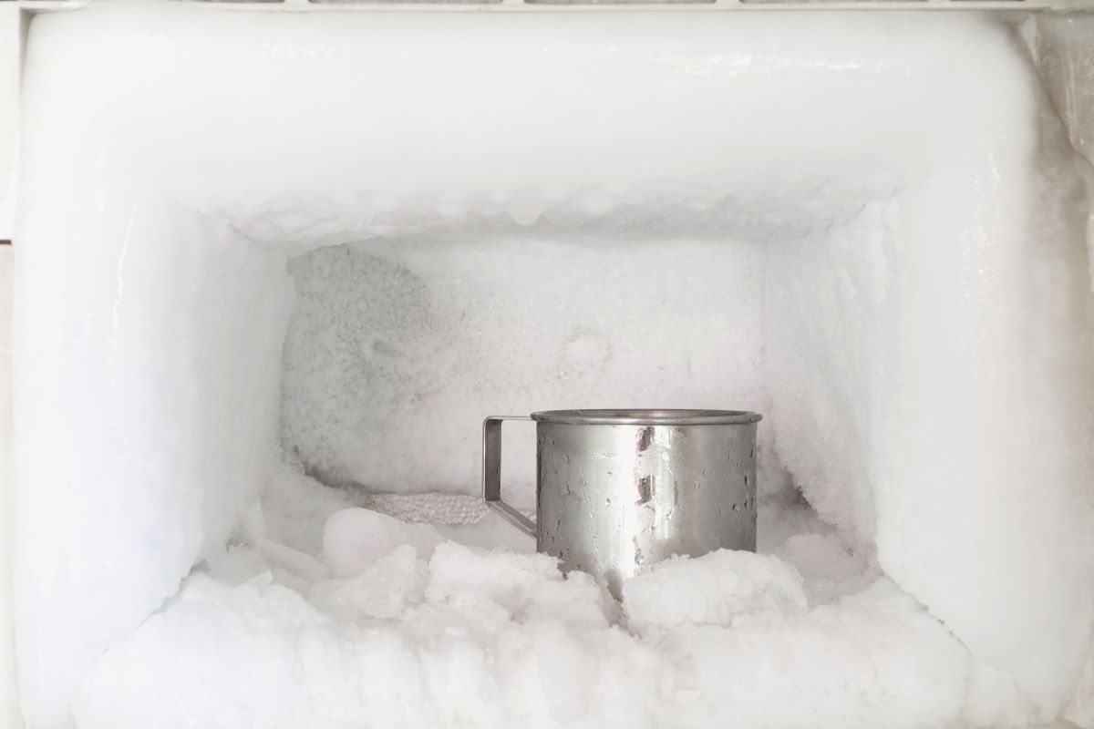 Stainless steel drinking water glass in freezer of a refrigerator. Ice buildup inside of a freezer walls.
