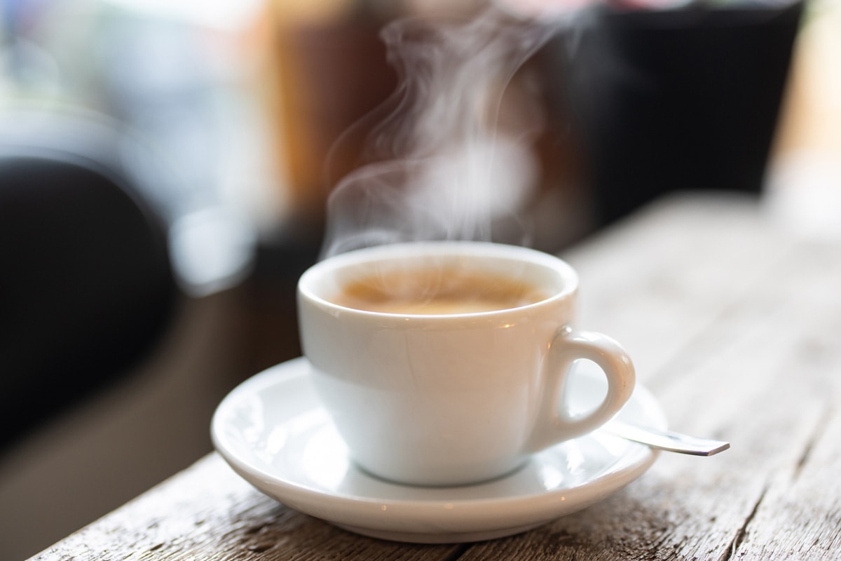 Steam rising from a white cup of hot coffee with a spoon on a saucer over a wooden table 
