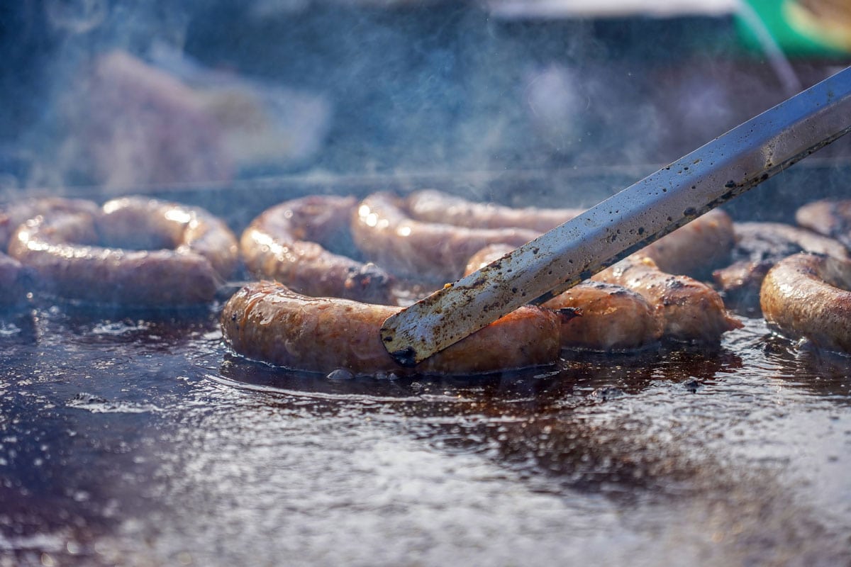 Street Food Vendor Turning Sausages With Barbecue in griddle