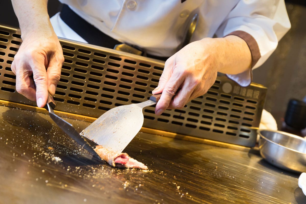 Teppanyaki japanese plate chef flipping some sliced meat on a spacious griddle