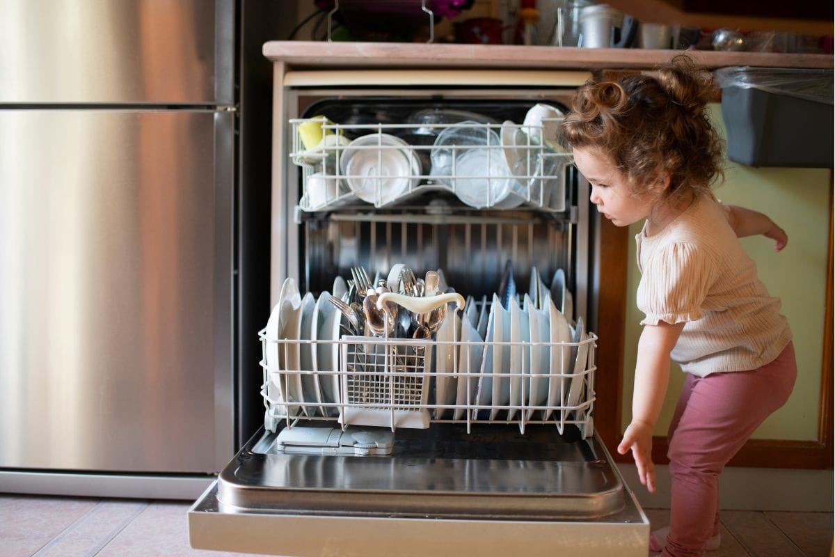 To help toddler, girl, mom, put dirty dishes in the dishwasher at home. Cute little baby girl dishwasher, the concept of the importance of water