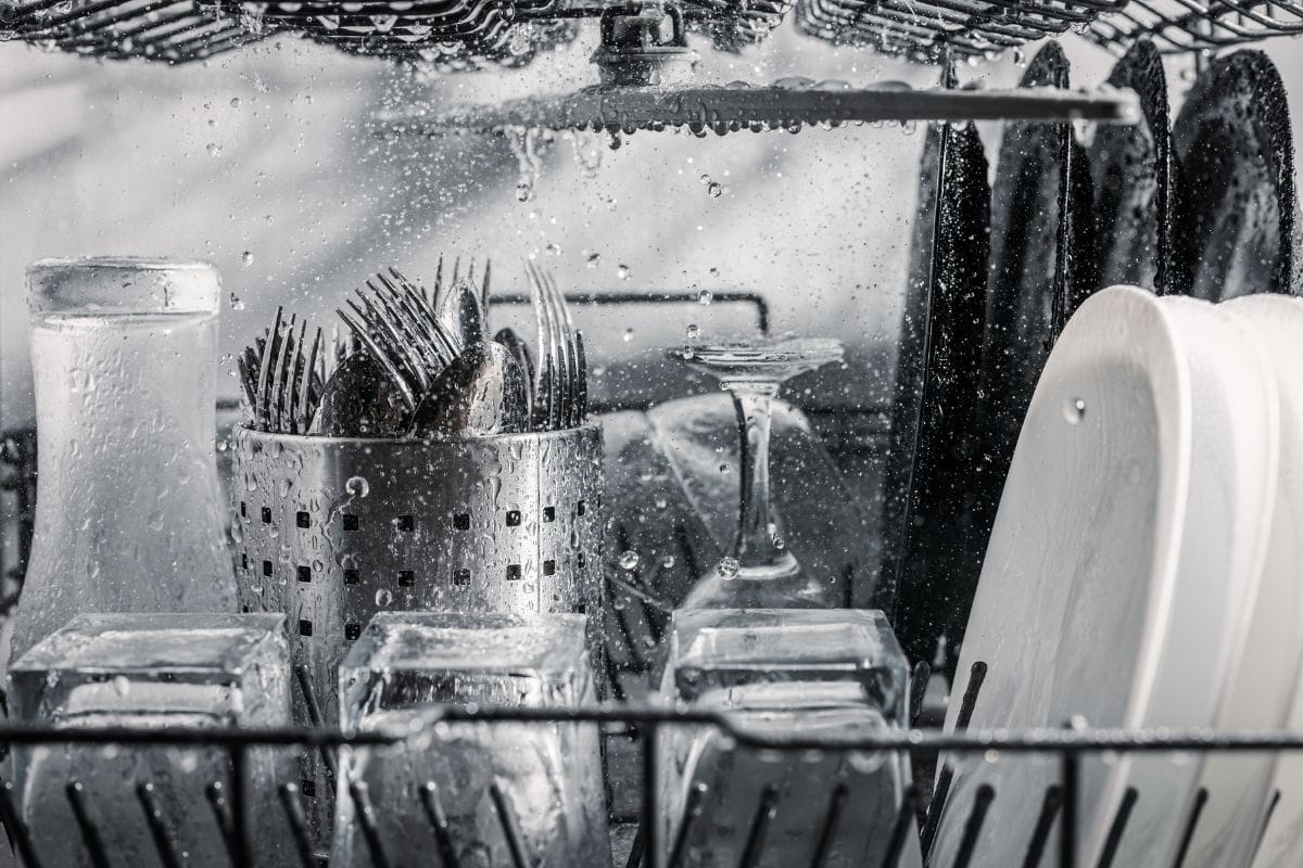 Transparent-and-black-and-white-dishes-as-well-as-cutlery-and-glasses-are-washed-in-the-dishwasher-inside-view-drops-and-splas