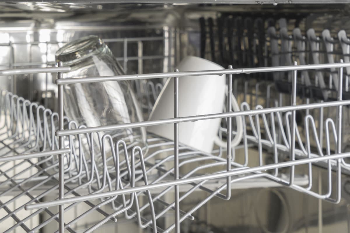 Washed glass and white mug in the dishwasher, the interior of the top rack of a dishwasher
