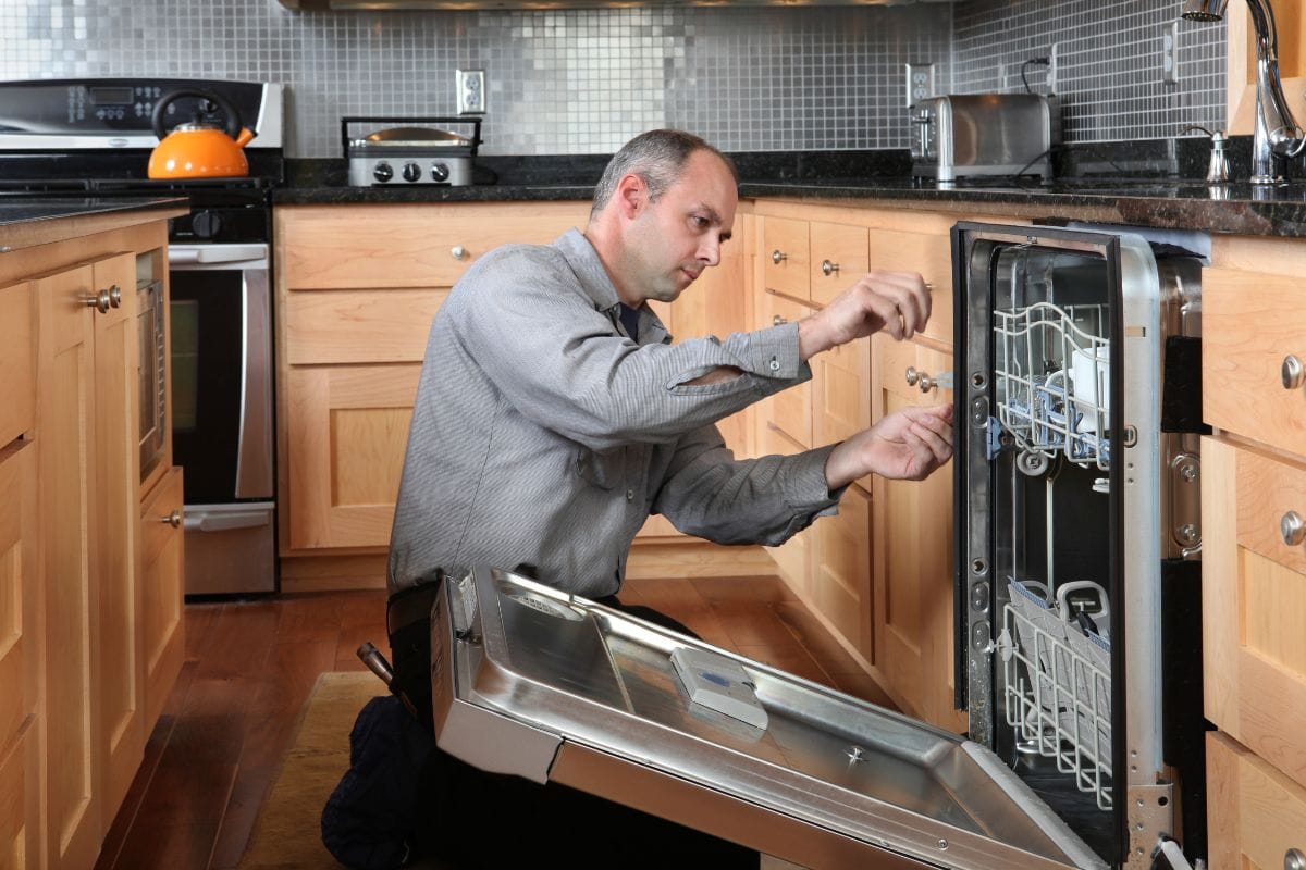Worker repairing energy efficient dishwasher in beautiful, contemporary kitchen.