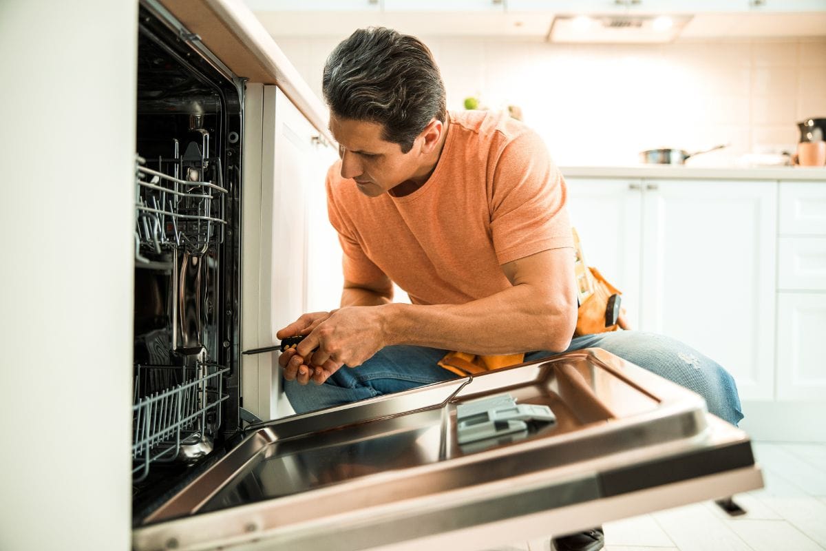 Worker using screwdriver to repair dishwasher at home stock photo