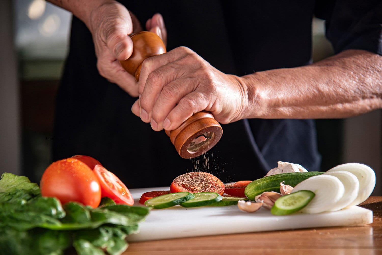 man using pepper grinder for cooking vegetable salad