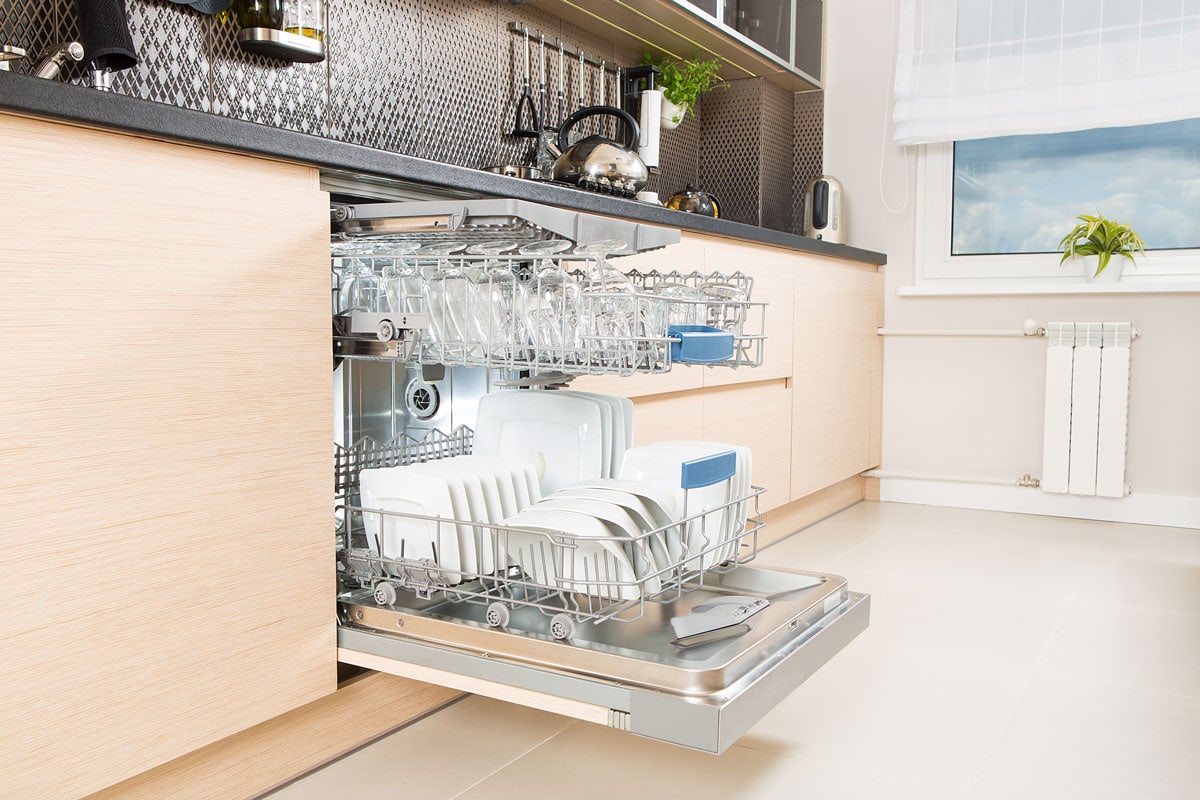 modern kitchen with dishwasher opened full of plates and glass