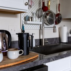 A black Stanley French press next to a water heater and coffee mugs, How To Use A Stanley French Press [Step By Step Instructions]