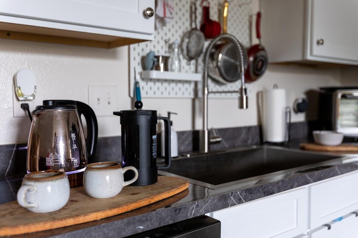 A black Stanley French press next to a water heater and coffee mugs