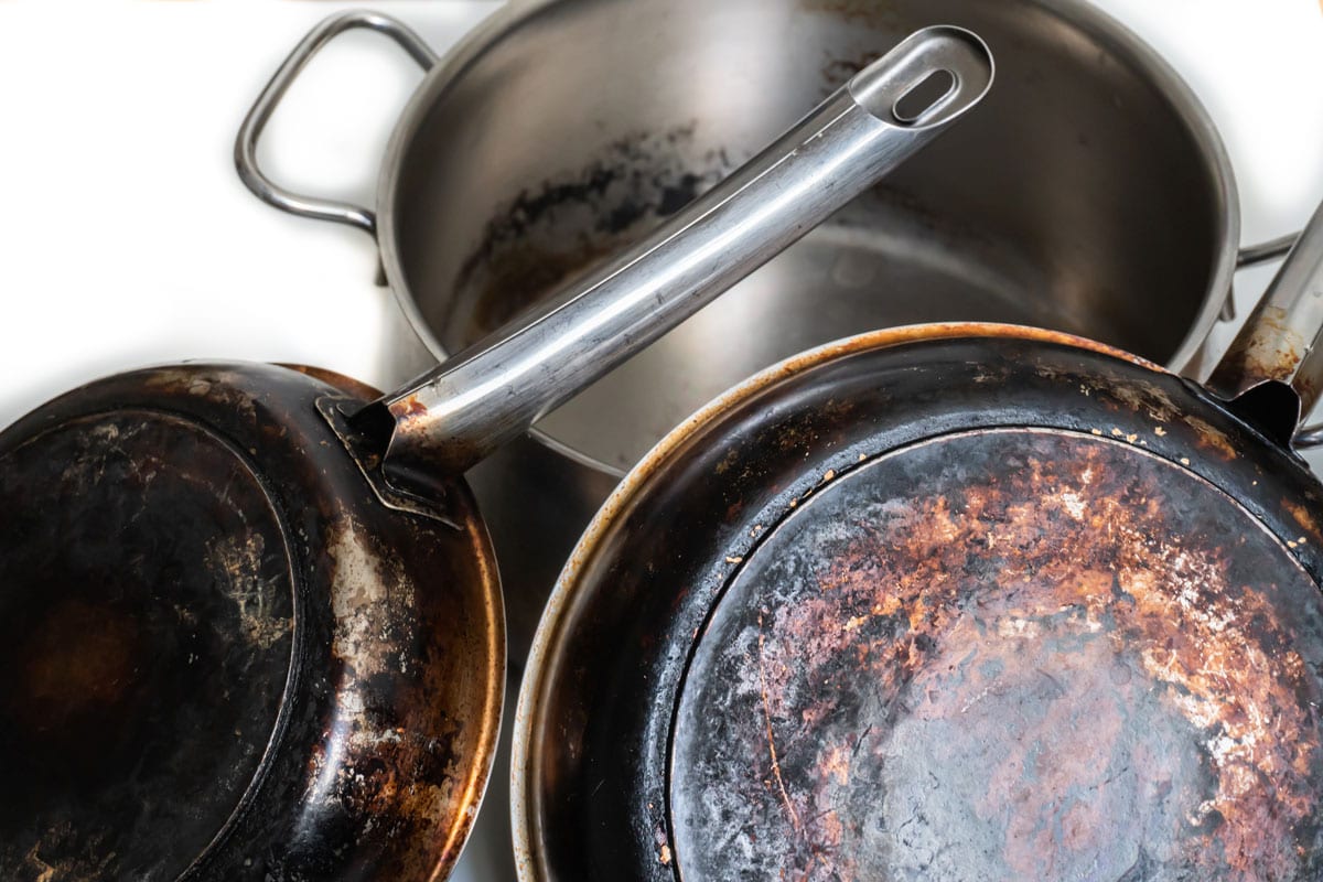 A composition of burnt and dirty, stainless steel pots and pans