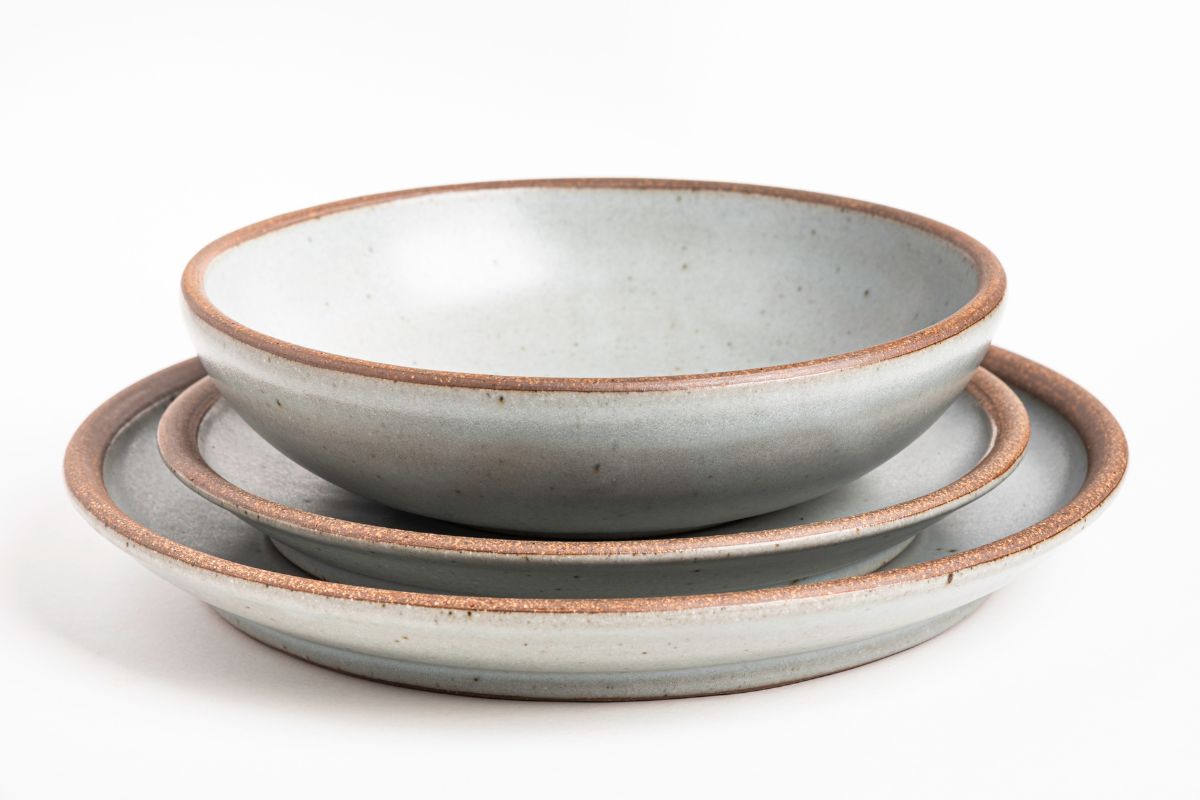 A set of stoneware dinner service with different plates and bowls on a white plain background.