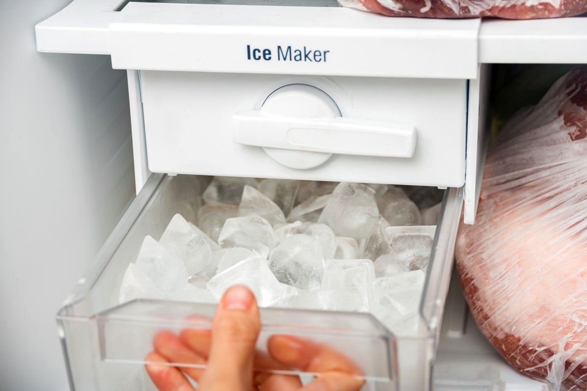 A woman opens an ice maker tray in the freezer to take ice cubes to cool drinks
