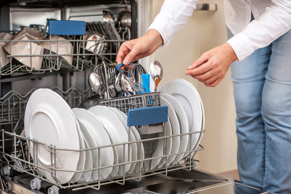 Adult Woman Unloading Dishwasher In The Kitchen 
