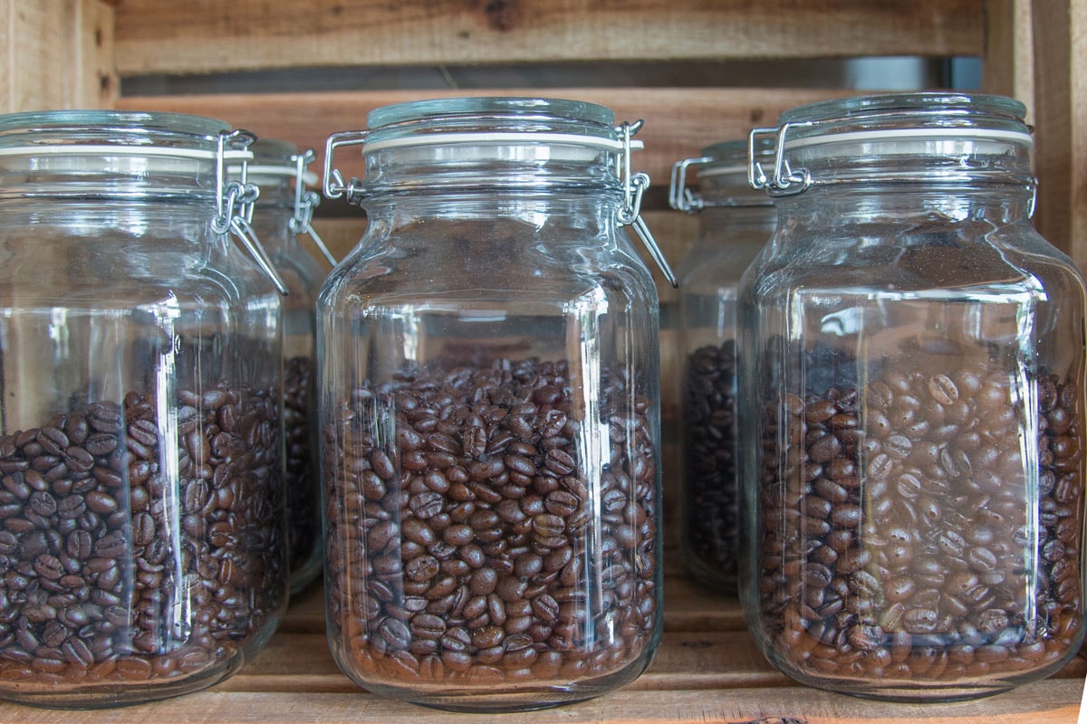 Coffee beans into a glass pot beside other one with natural roasted coffee beans