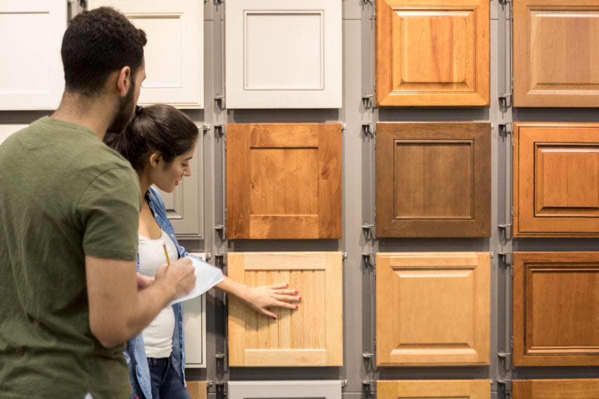 Couple look at cabinet samples in a hardware store. The woman touches one of the cabinet samples. The man is taking notes.