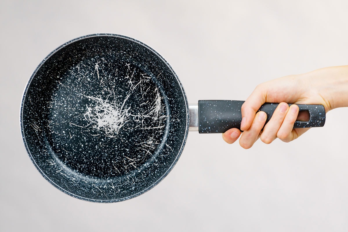Hand holding scratched frying pan, cause of cancer. Torn coating, kitchen utensil is unusable