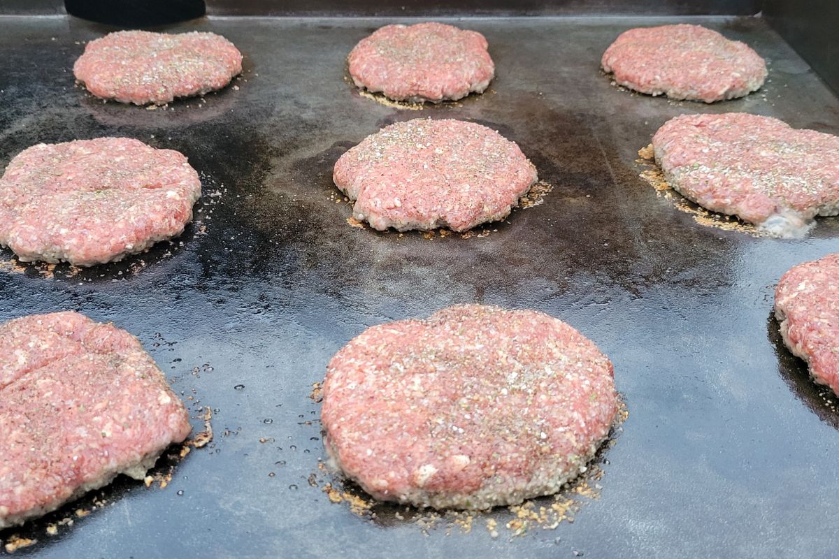 Lots of raw beef seasoned burgers grilling on a seasoned griddle in Florida