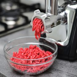 Meat grinder with fresh forcemeat on kitchen table. Side view of a meat grinder and minced meat falling into a glass bowl. Selective focus. - Can You Grind Cooked Meat In A Meat Grinder Or Blender