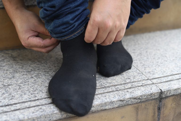 Man at home in morning puts gray socks on his leg, Is Dirty Sock Syndrome Dangerous? [And How Homeowners Can Fix It]