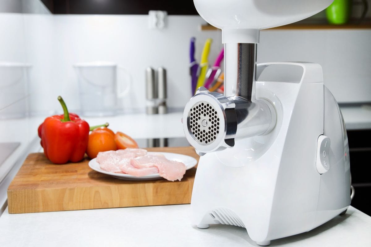Meat grinder in modern kitchen. Vegetables in background