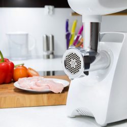 Meat grinder with fresh meat on a wooden table in kitchen interior. - Can I Use A Meat Grinder For Tomatoes?