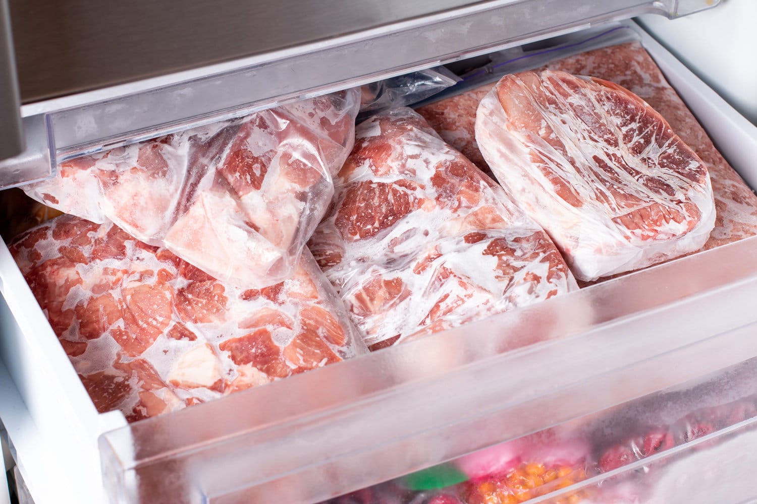 Meat in refrigerator freezer background. Closeup pork, meat and chicken leg in freezing compartment. Frozen food