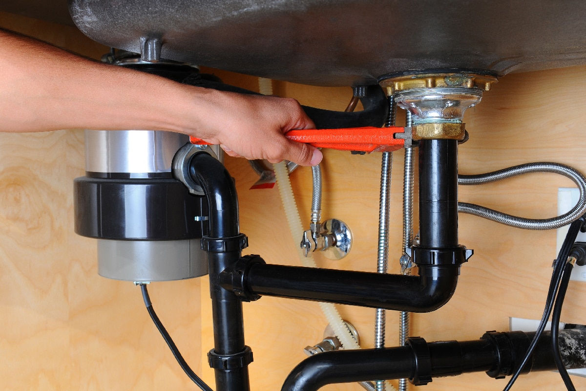 Plumber using a wrench to tighten a fitting beneath a kitchen sink