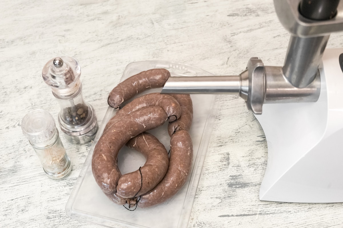 Raw fresh homemade beef sausages in a natural shell on a wooden table close up. Meat grinder for cooking minced meat and jars of spices. Fast and nutritious food for picnics and barbecues.