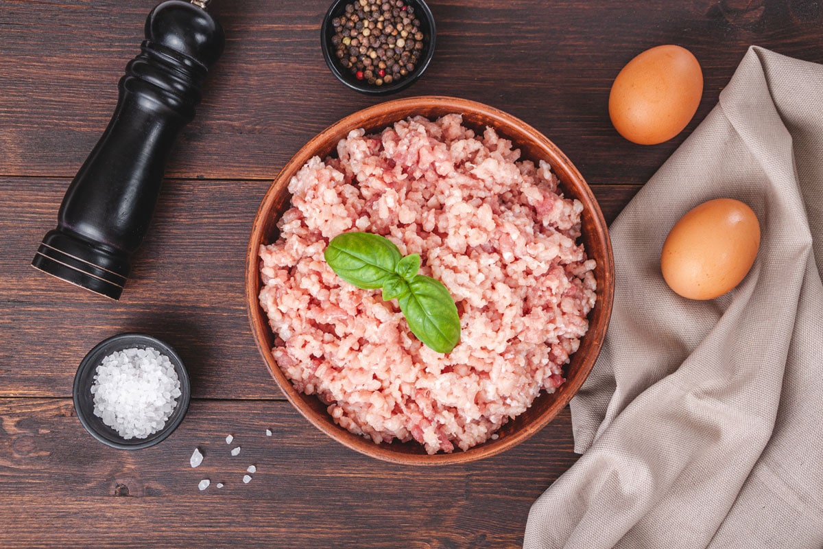 Raw minced meat in bowl on wooden table and ingredients