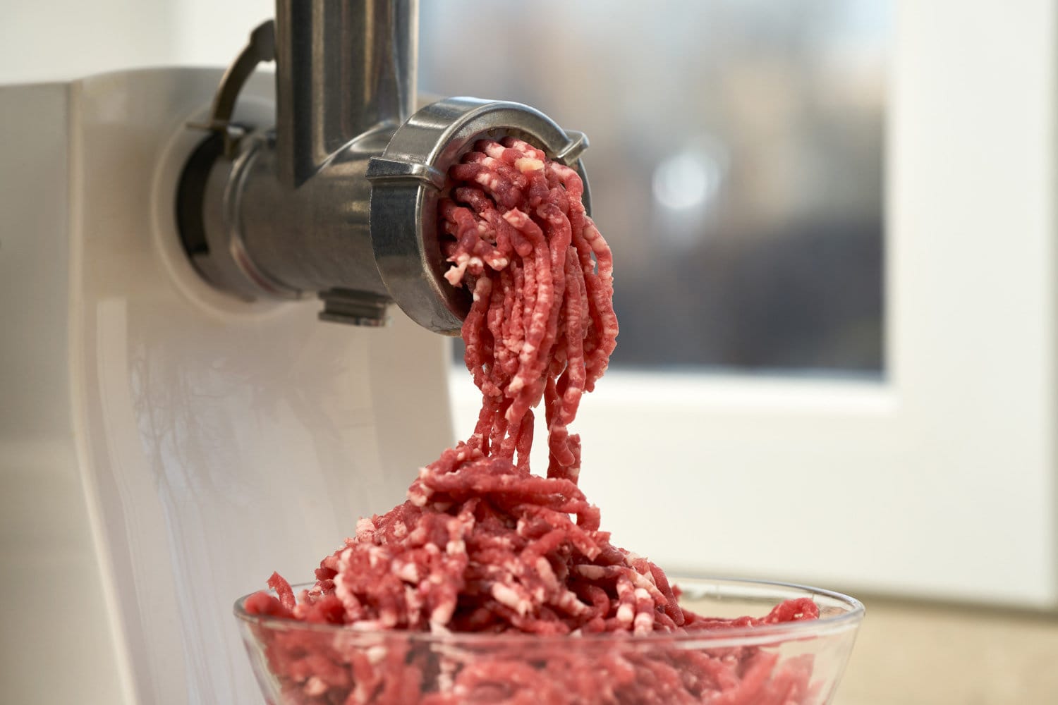 Side view of a meat grinder and minced meat falling into a glass bowl. Selective focus.