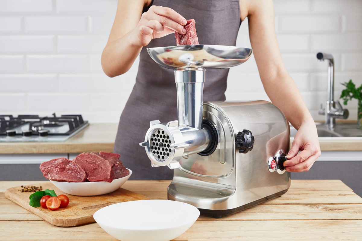 The process of preparing forcemeat by means of a meat grinder. Female hands use meat chopper at kitchen.