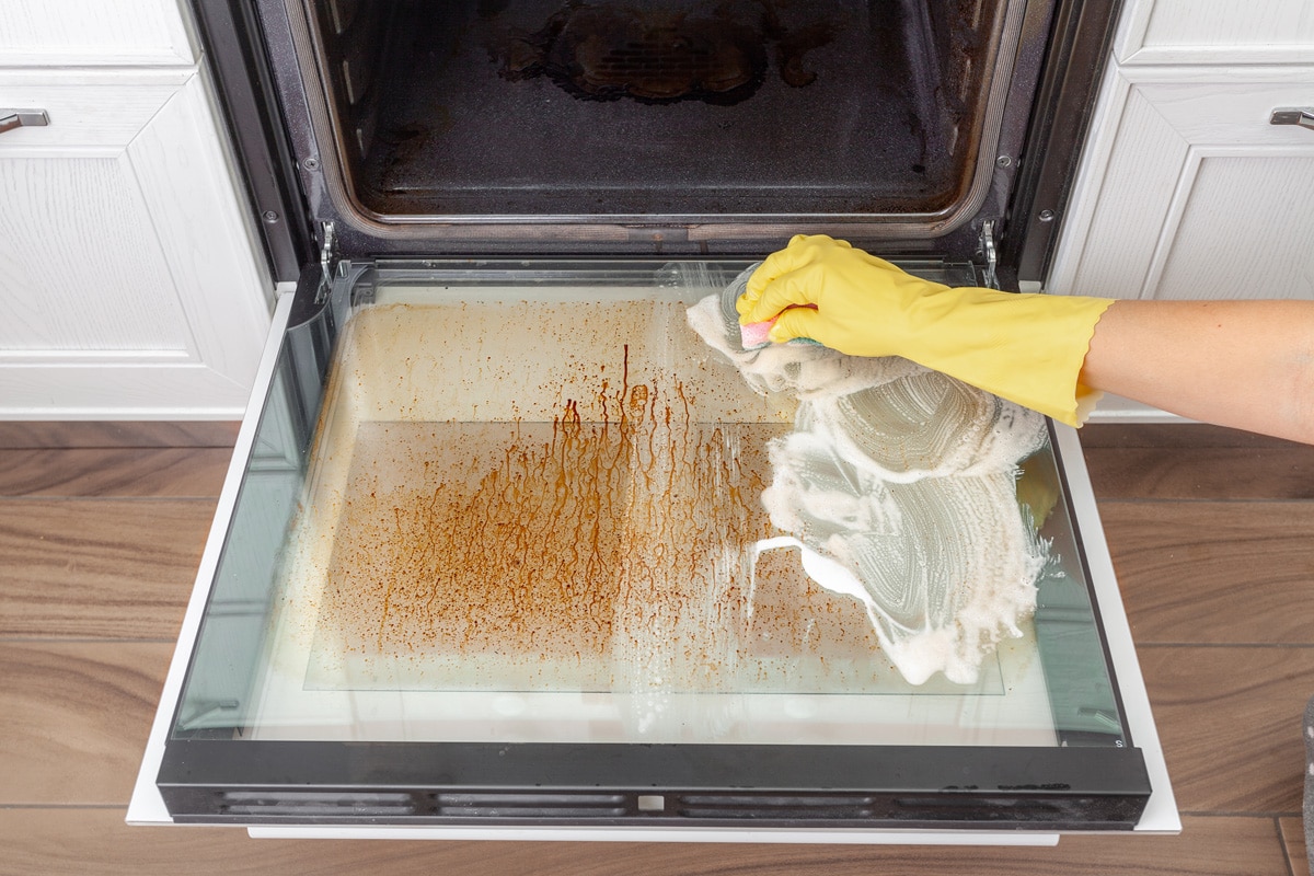 Woman cleaning the glass window of the oven due to stain
