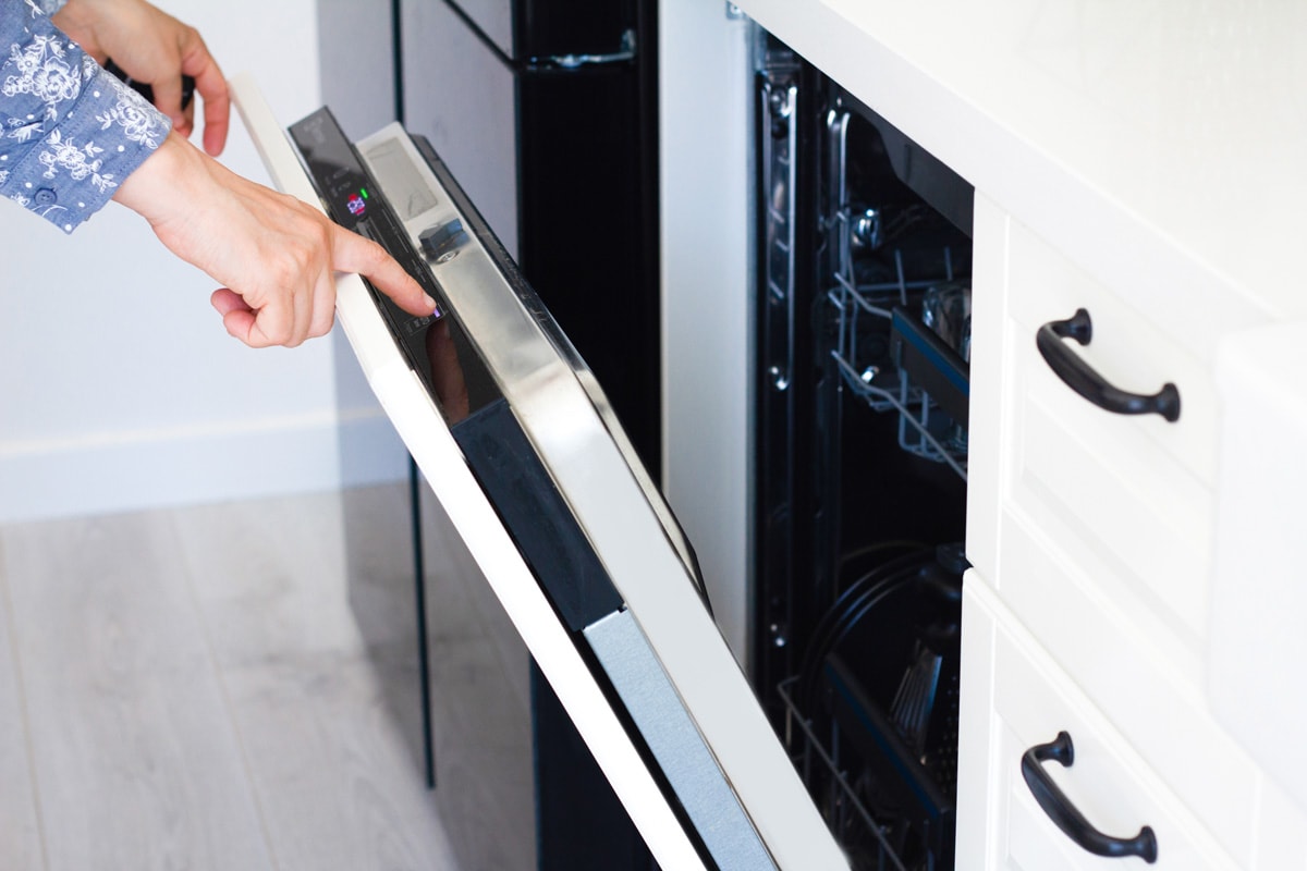 female hand is switching on off a modern built-in dishwasher