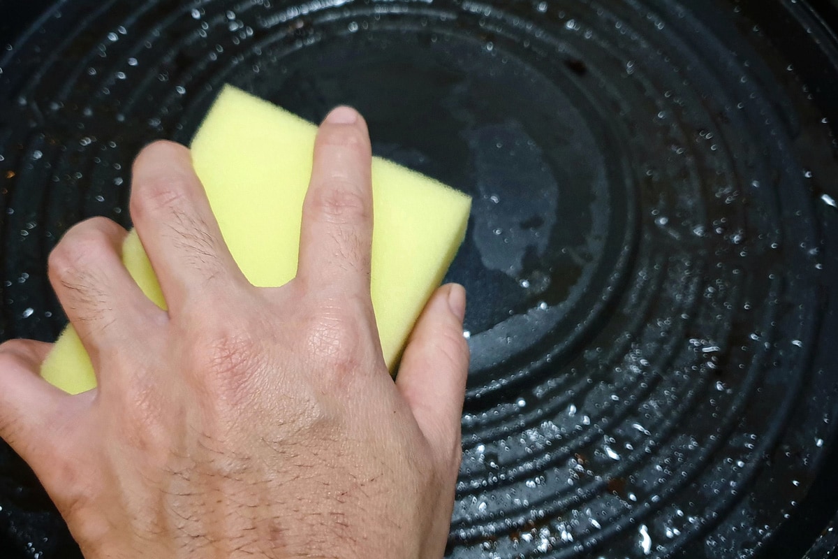 housewife woman's hand holding cleaning sponge scrub for wash the dirty frying pan with a pattern of grease and oil stains