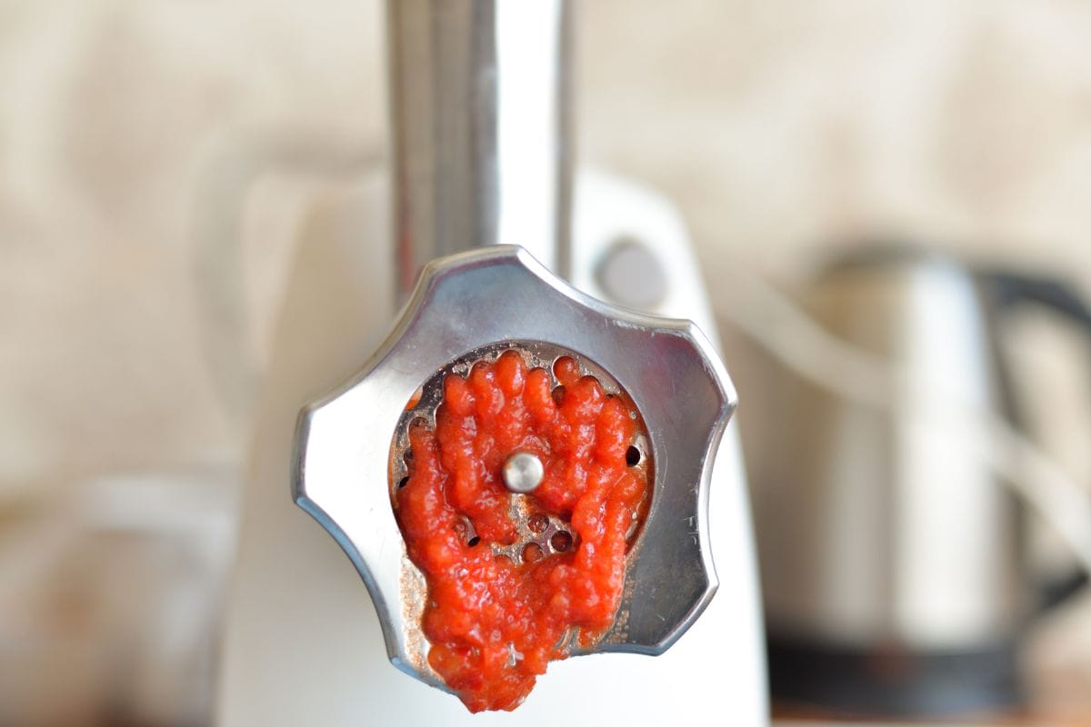 the process of grinding red tomatoes in a meat grinder