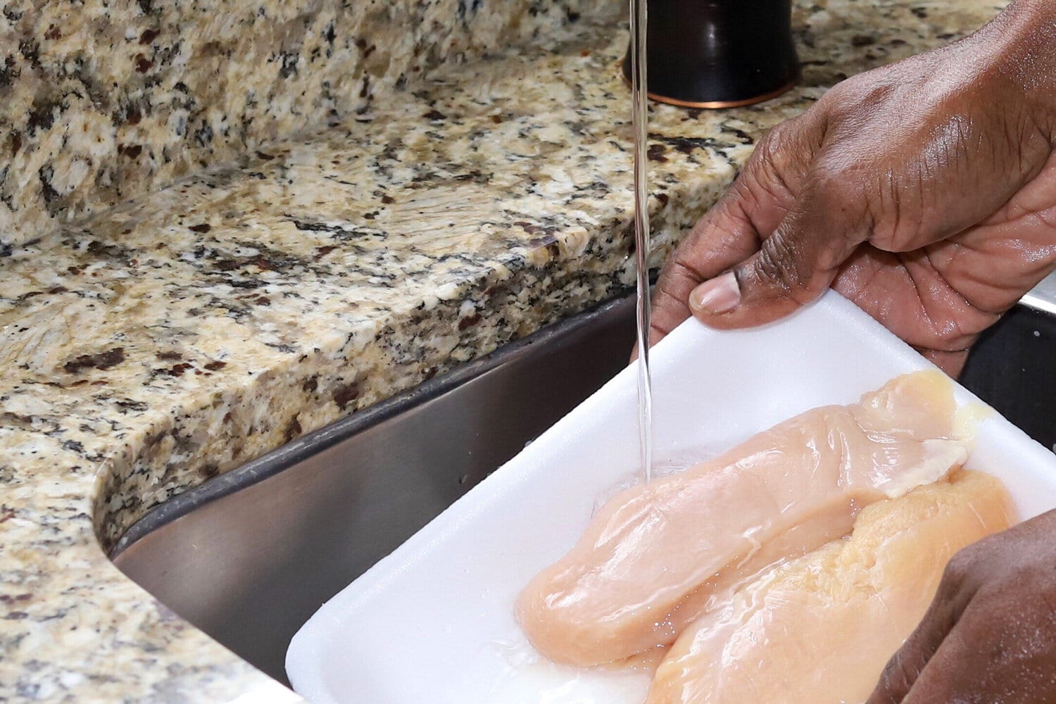 A close up image of a African-American man hands cleaning organic chicken breast in a kitchen sinku