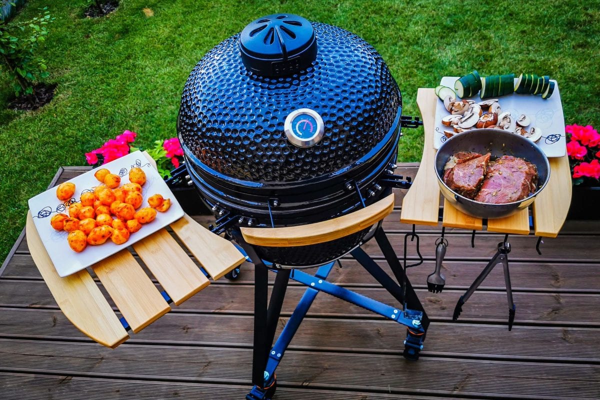 A kamado egg type barbeque grill standing on a living house terrace with beef steaks and vegetables to be cooked.