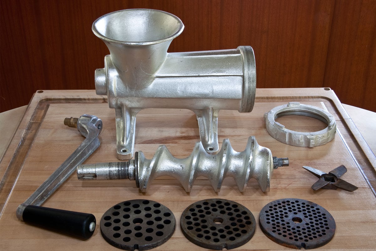 A standard meat grinder disassembled into its component pieces including the body,