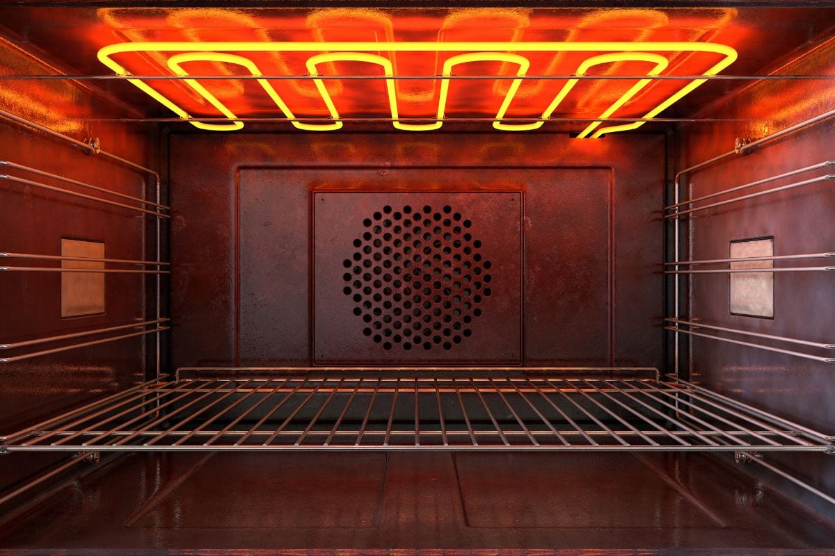 An upclose view through the front of the inside of an empty hot operational household oven with a glowing element and metal rack -
