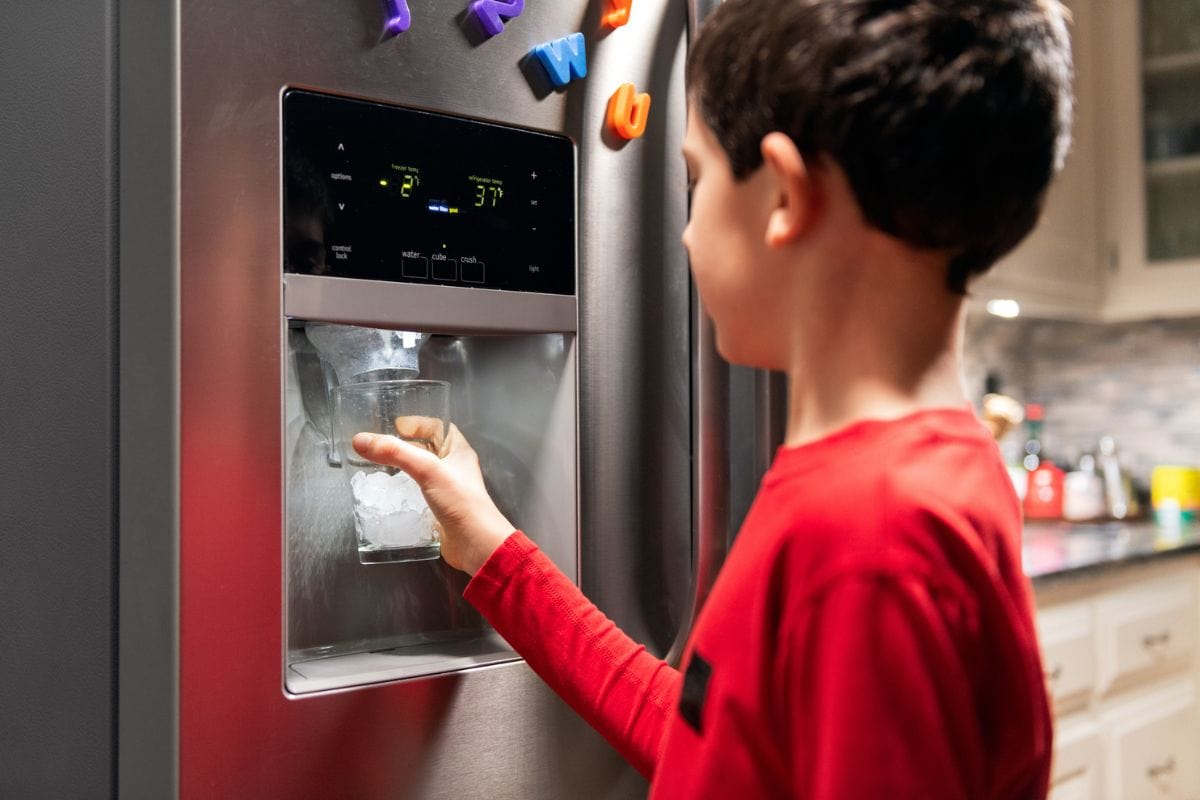 Boy filling glass with ice from Refrigerator Ice maker