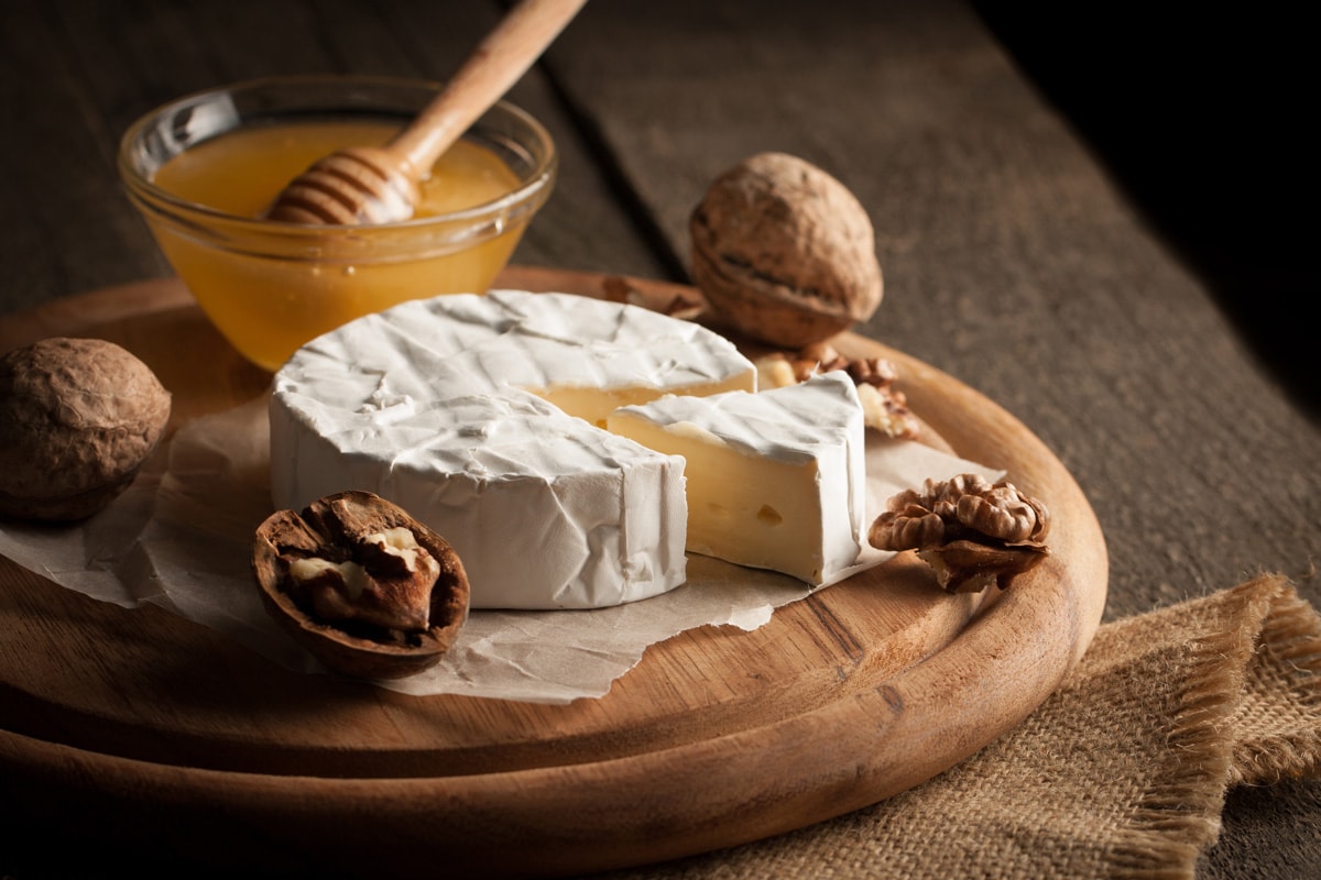 Camembert and brie cheese on wooden background with nuts spices and garlic.