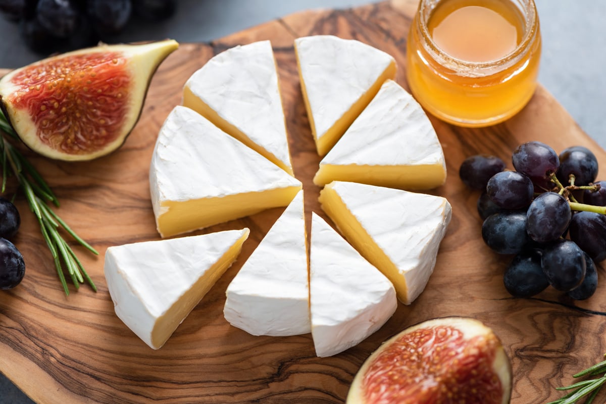 Camembert or brie cheese with figs, grapes and honey on wooden serving board