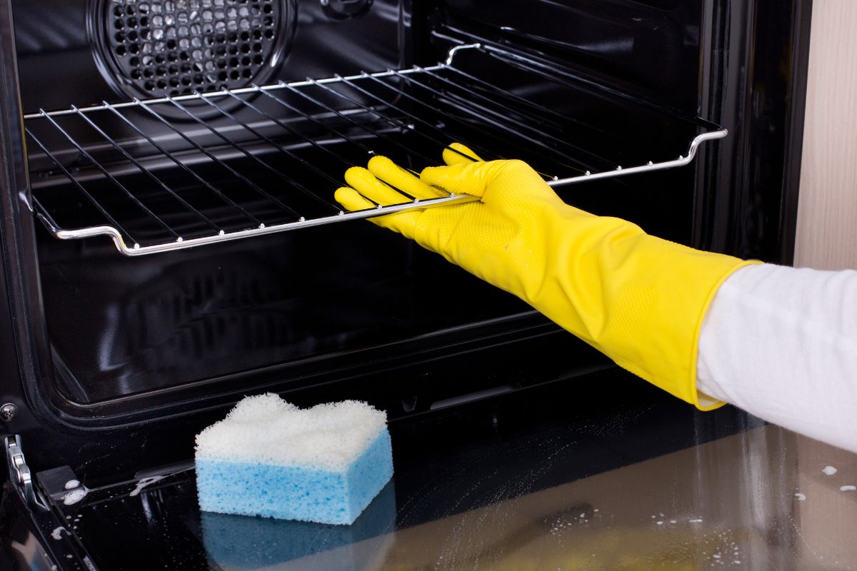 Close up of female hand with yellow protective gloves cleaning oven