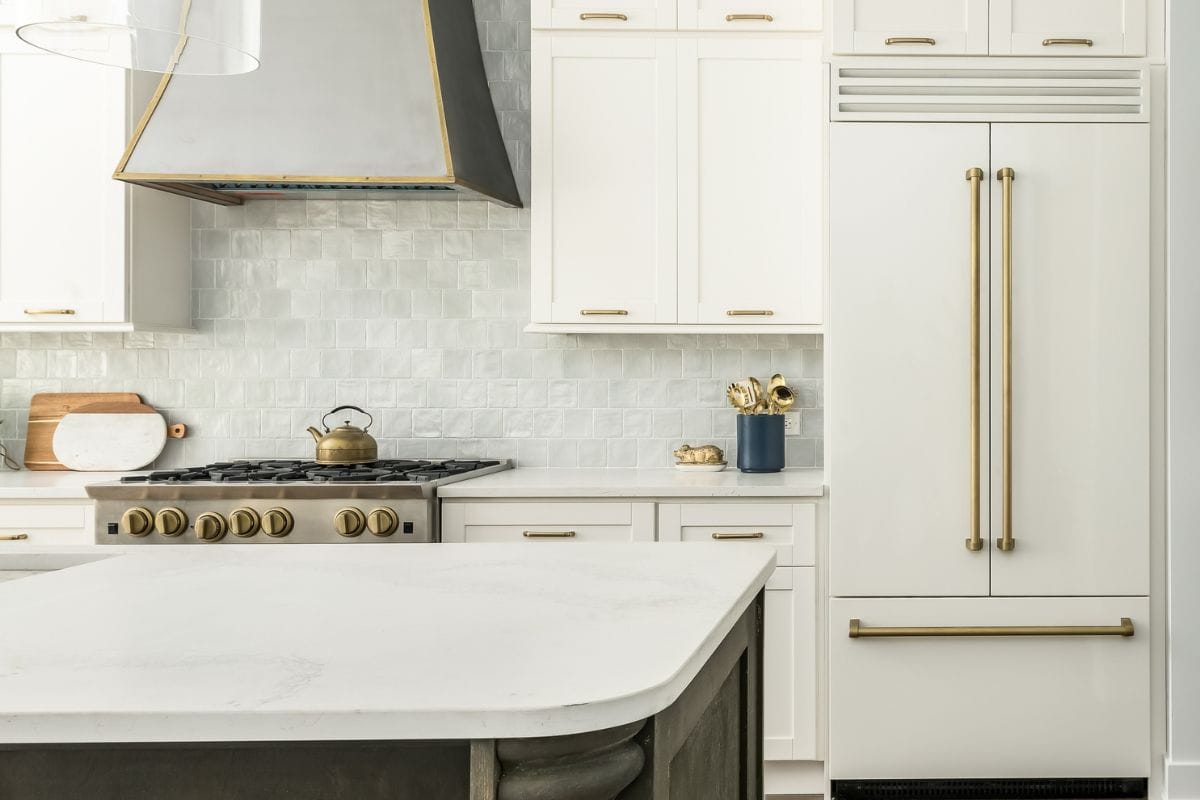 Elegant Kitchen Design with white matte refrigerator, white cabinets, and two toned kitchen island. Gray tile backsplash and metal range hood.