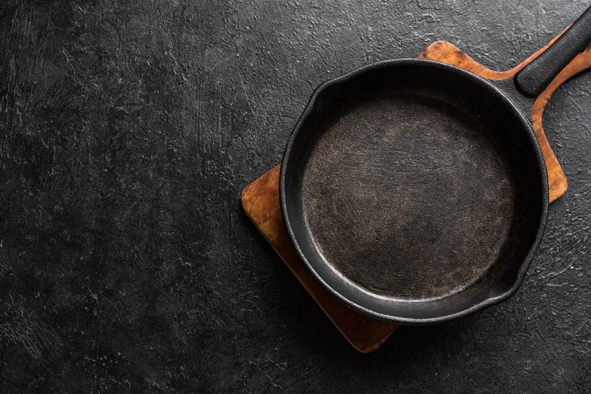 Empty cast iron frying pan for cooking on black background, top view, copy space. Cooking concept background with black pan