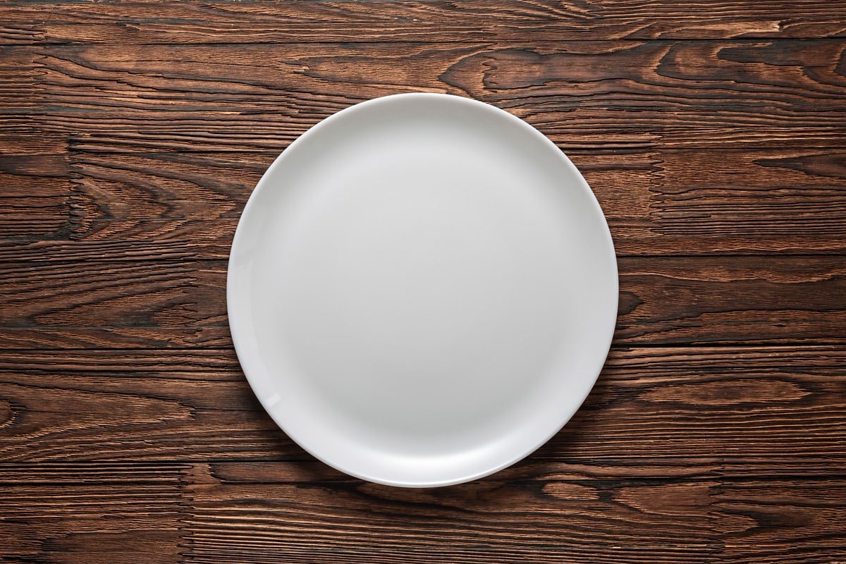 Empty white plate on a wooden table.