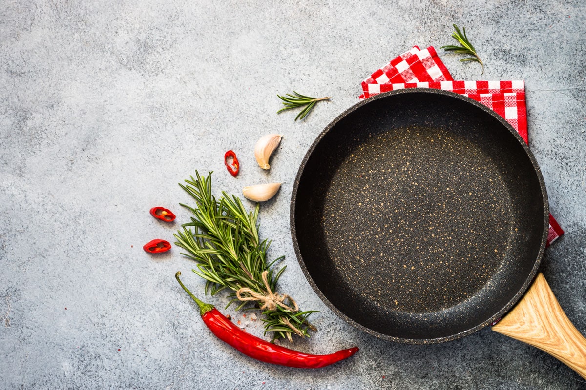 Food cooking background with Frying pan or skillet, spices and herbs on gray stone table