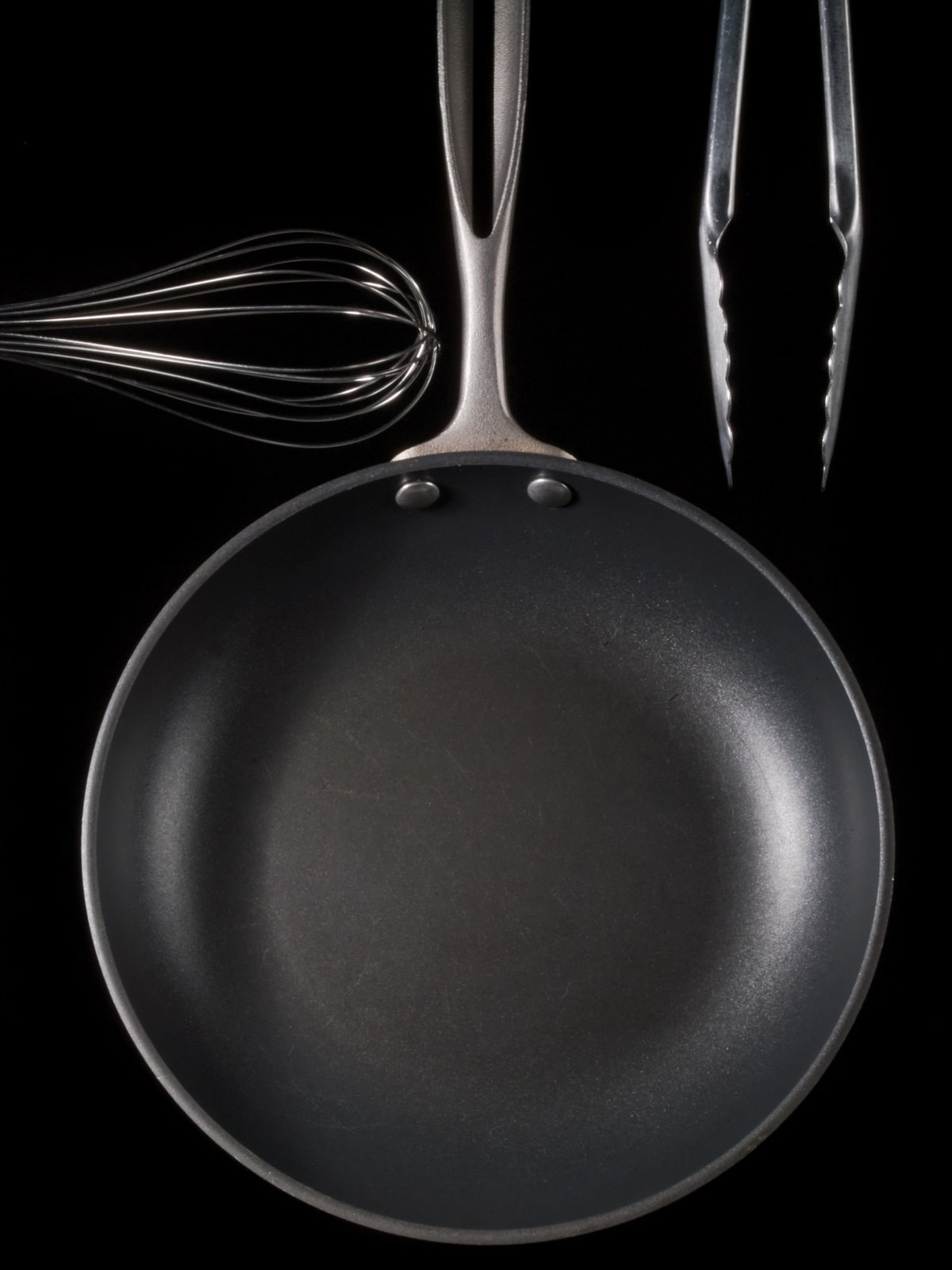 Frying pan, whisk &amp pair of tongs on black background