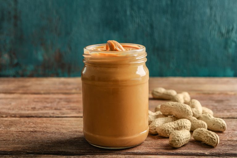 A glass jar with creamy peanut butter on wooden table, Can Peanut Butter Go Bad In Heat? [Yes! Here's How To Tell If It's Spoiled!]
