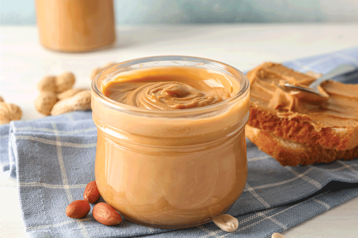 Glass jar with peanut butter, peanut, kitchen towel, spoon and peanut butter sandwich